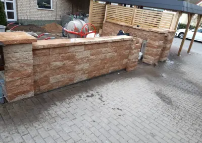 Gartenmauer aus Natursteinoptik-Blöcken auf gepflasterter Fläche