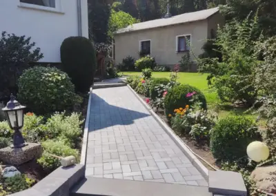 Gepflasterter Gartenweg mit Stufen und Mauereinfassung vor dem Haus