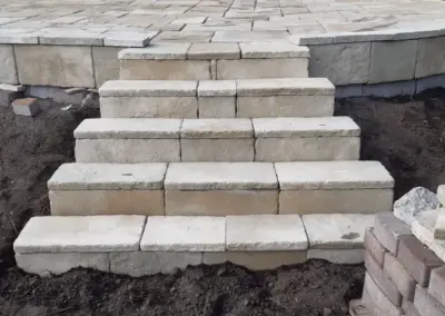 Treppe aus hellen Blockstufen zu einer Natursteinterrasse, im Bau