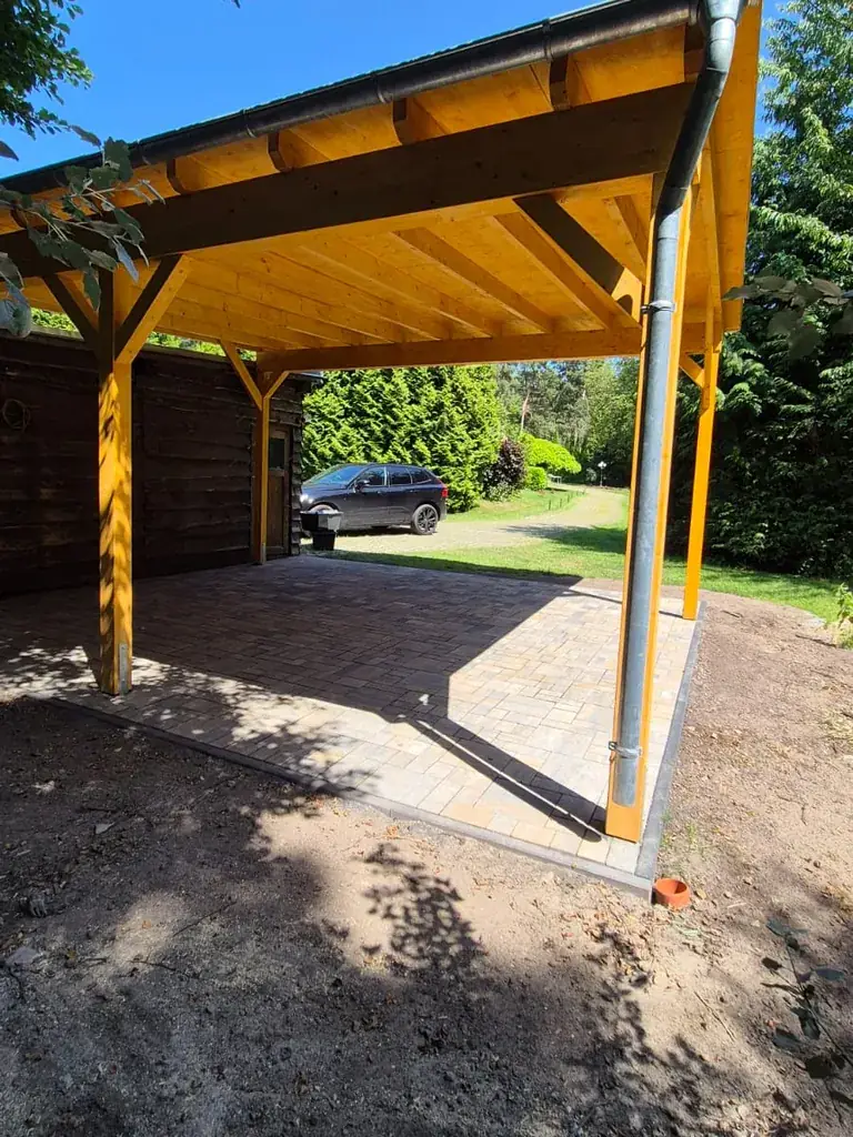 Holzcarport in Berlin-Spandau von der Seite: Pultdach mit Dachrinne und Fallrohr, daneben das Gartenhaus