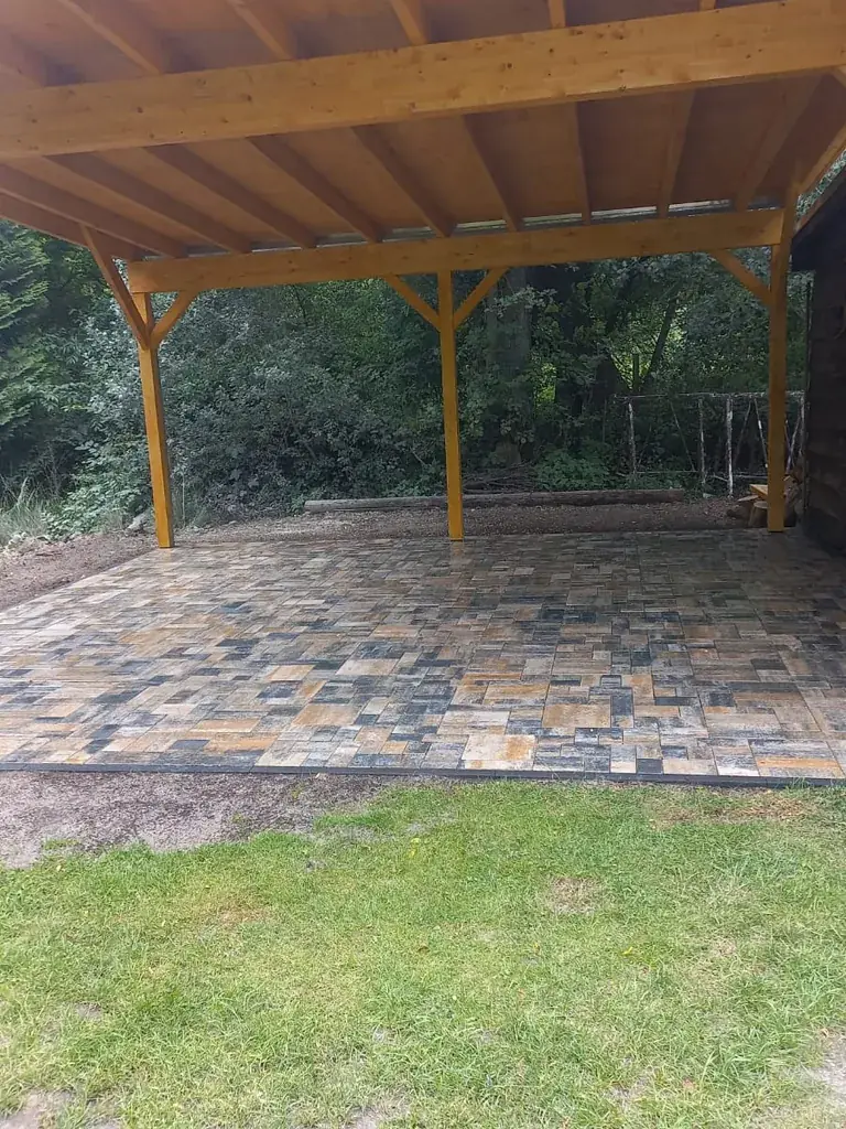 Gepflasterte Stellfläche unter dem Holzcarport mit dunkler Randeinfassung zum Rasen