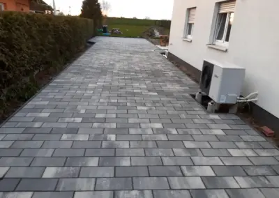 Breite Einfahrt aus grau-meliertem Betonpflaster entlang der Hauswand