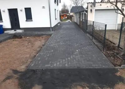 Einfahrt im Fischgrätverband aus anthrazitfarbenem Pflaster neben einem Neubau