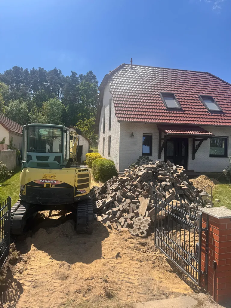 Minibagger beim Rückbau der alten Zufahrt, daneben ausgebaute Rasengittersteine