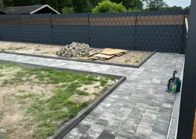 Anthrazitfarbener Sichtschutzzaun um einen Garten mit Pflasterfläche und Entwässerungsrinne